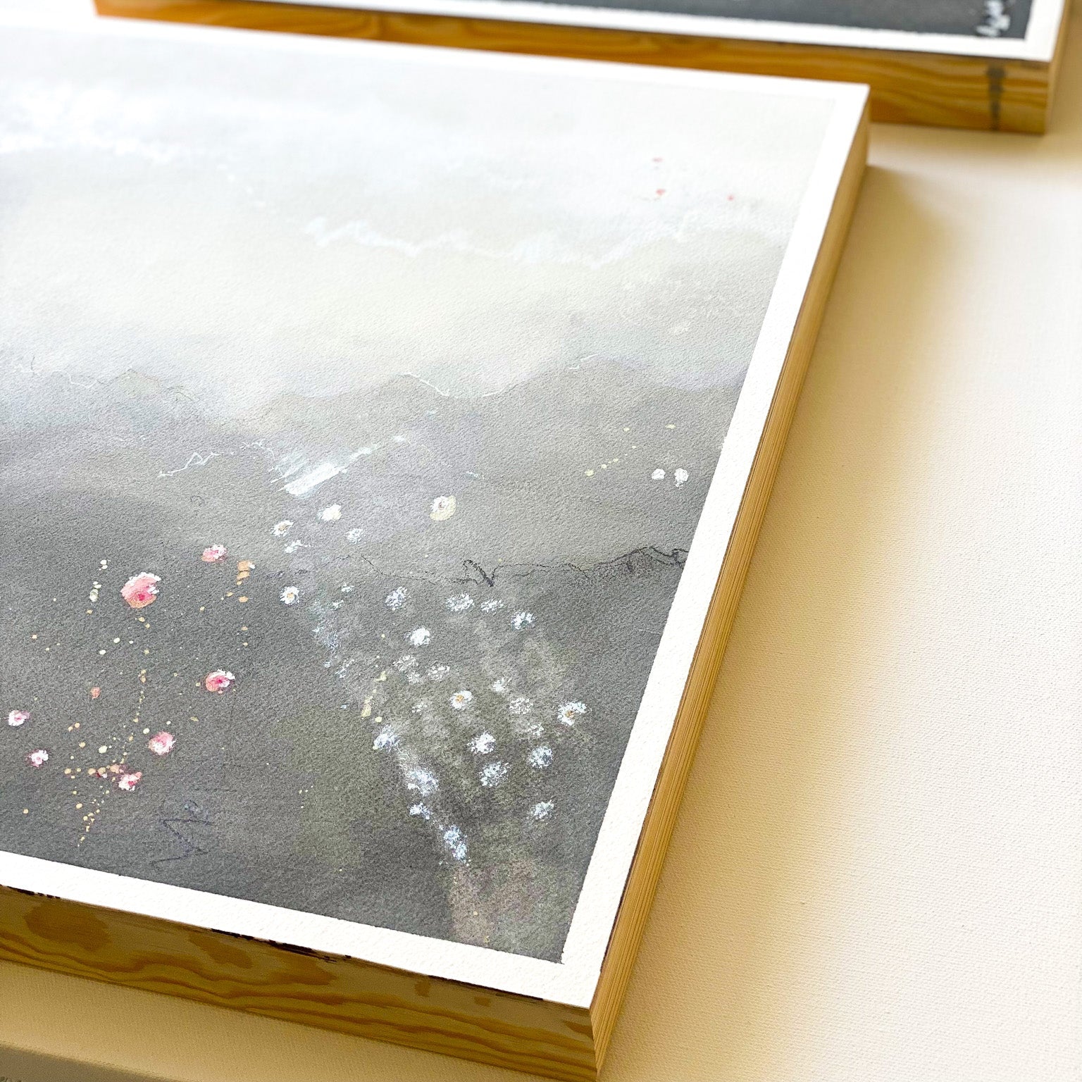 Two framed artworks on a light wooden surface