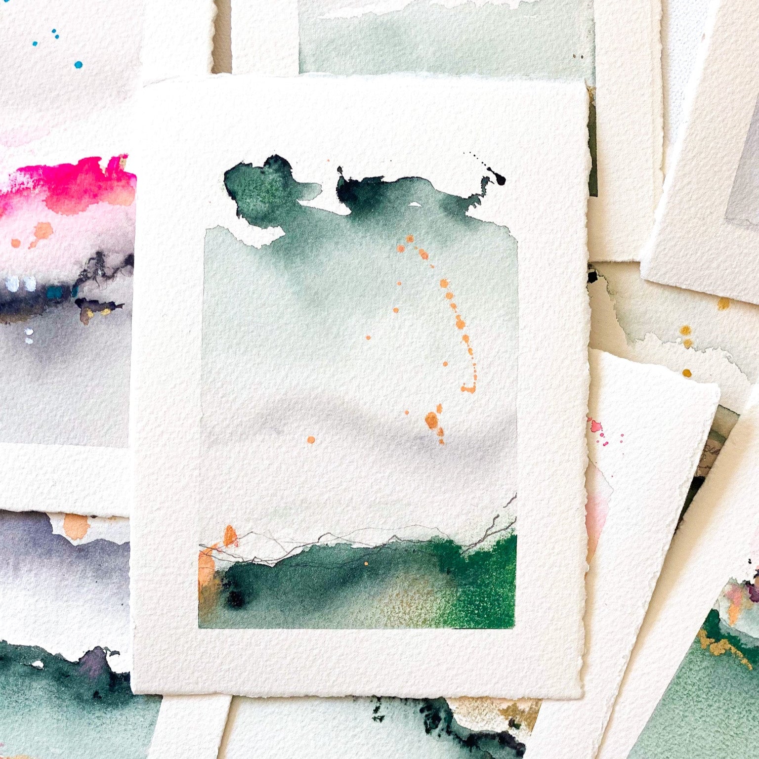 Stack of watercolor paintings with various colors and abstract designs.
