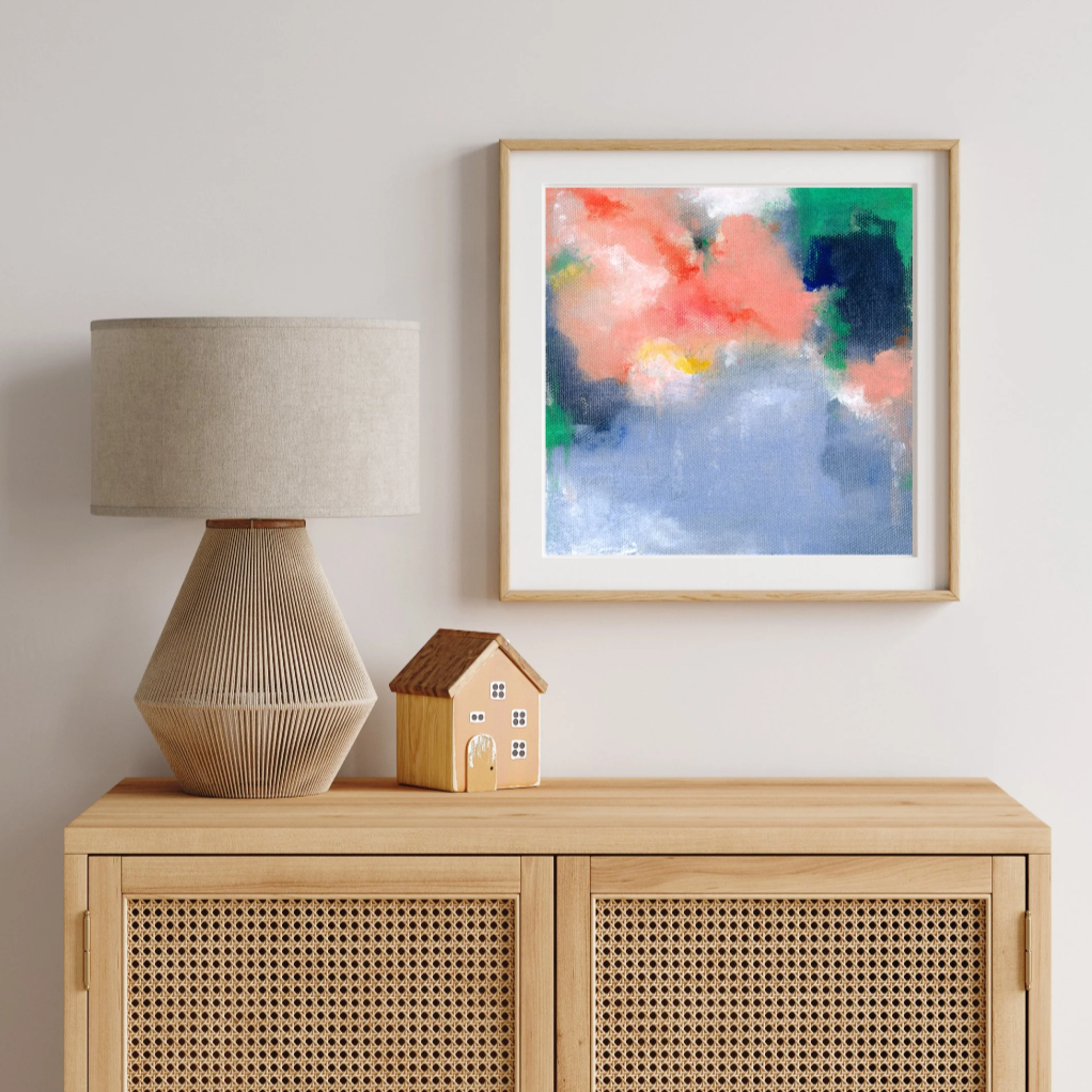 Decorative lamp, small house sculpture, and colorful abstract painting on a wooden cabinet against a light wall.