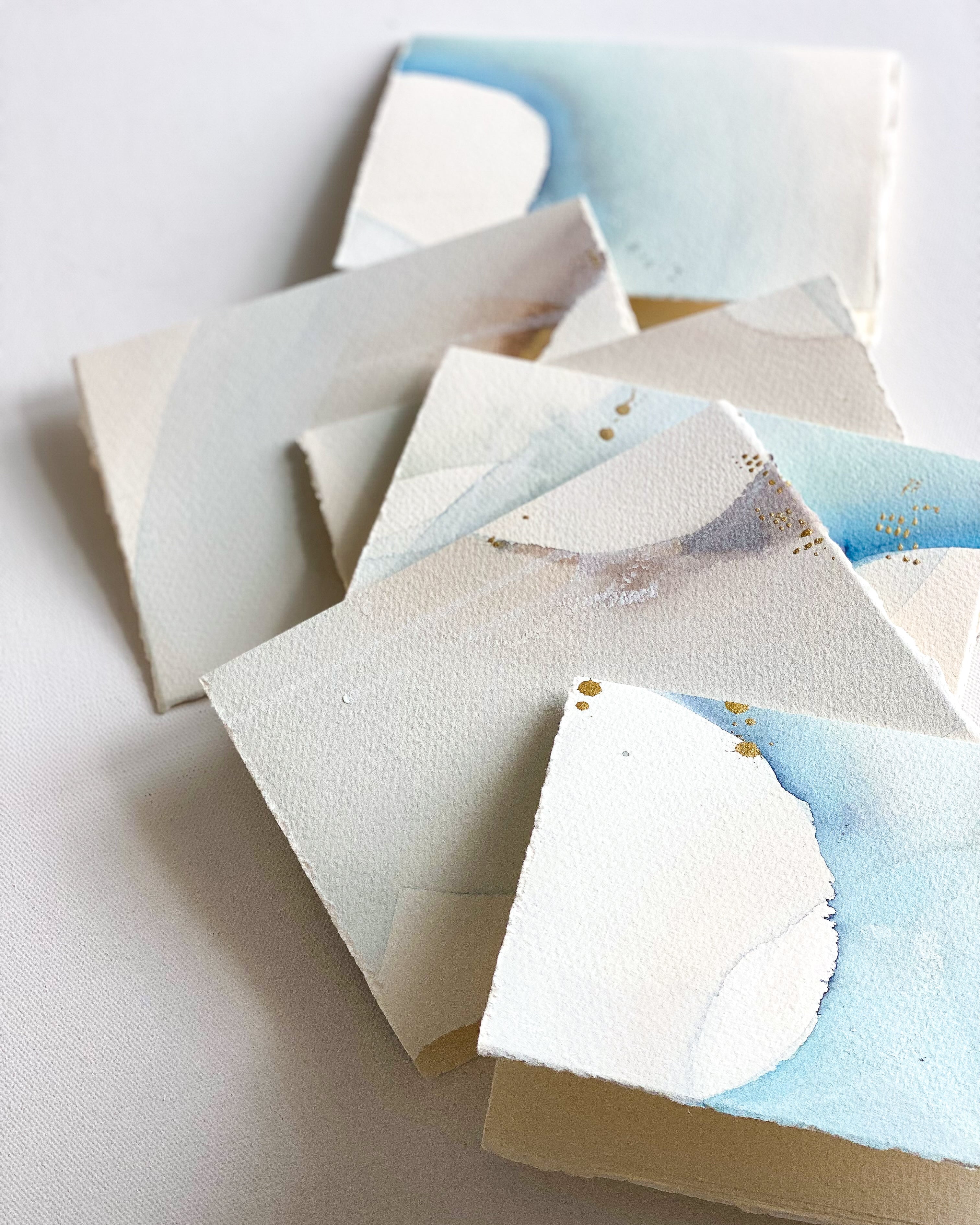 Stack of small notebooks with watercolor designs on a light background