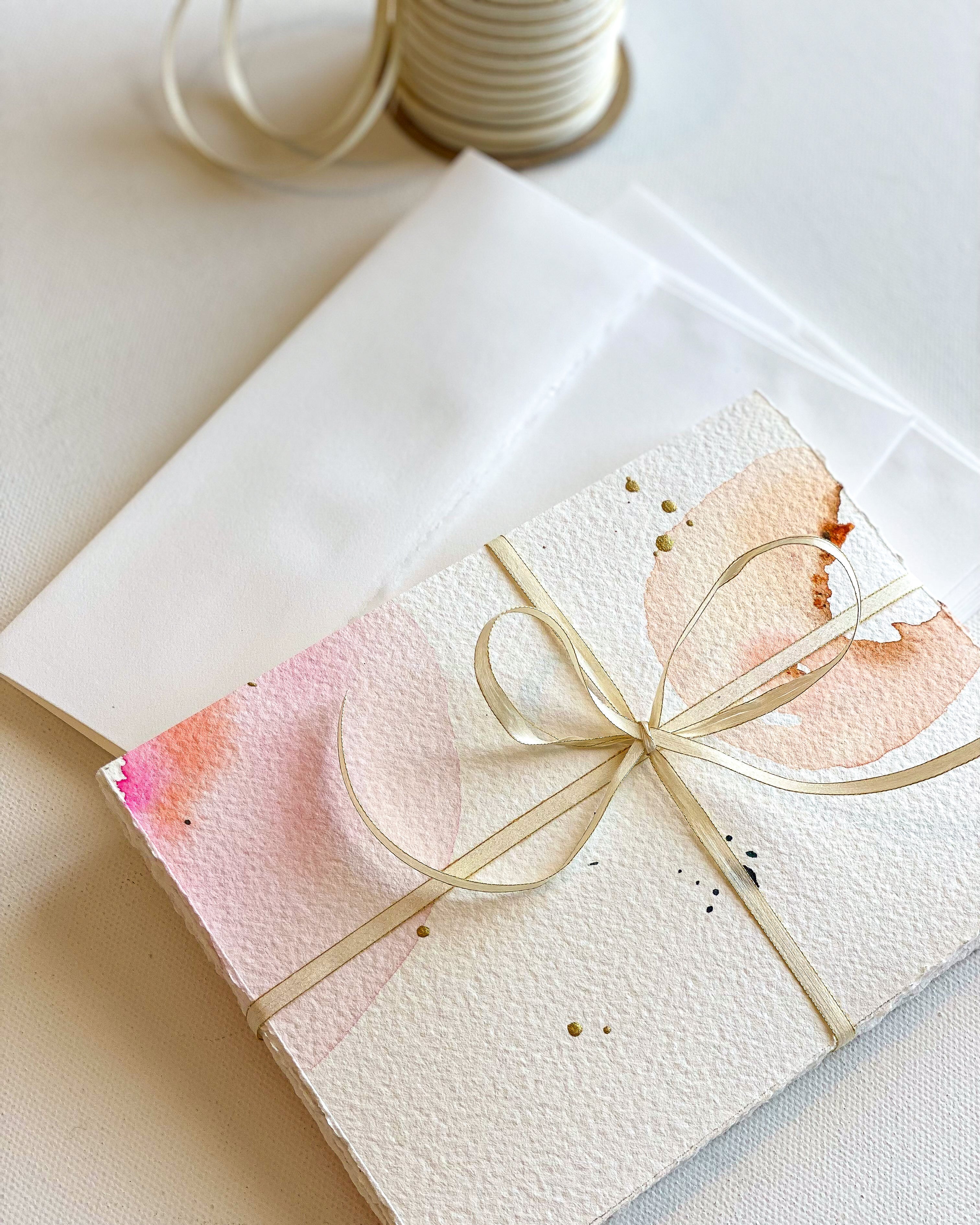 Stationery with watercolor design and gold ribbon on a white surface
