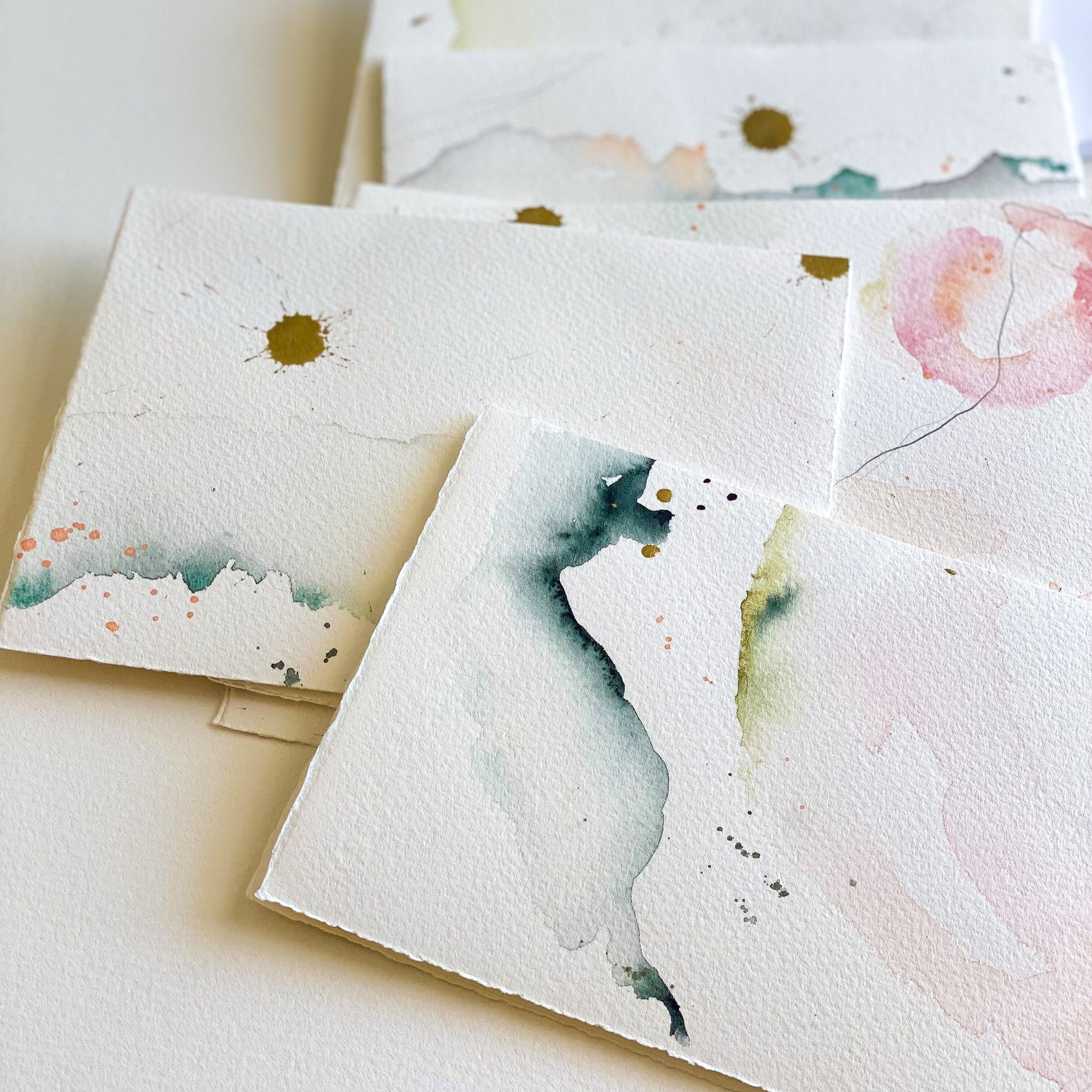 Set of watercolor cards with artistic designs on a white surface