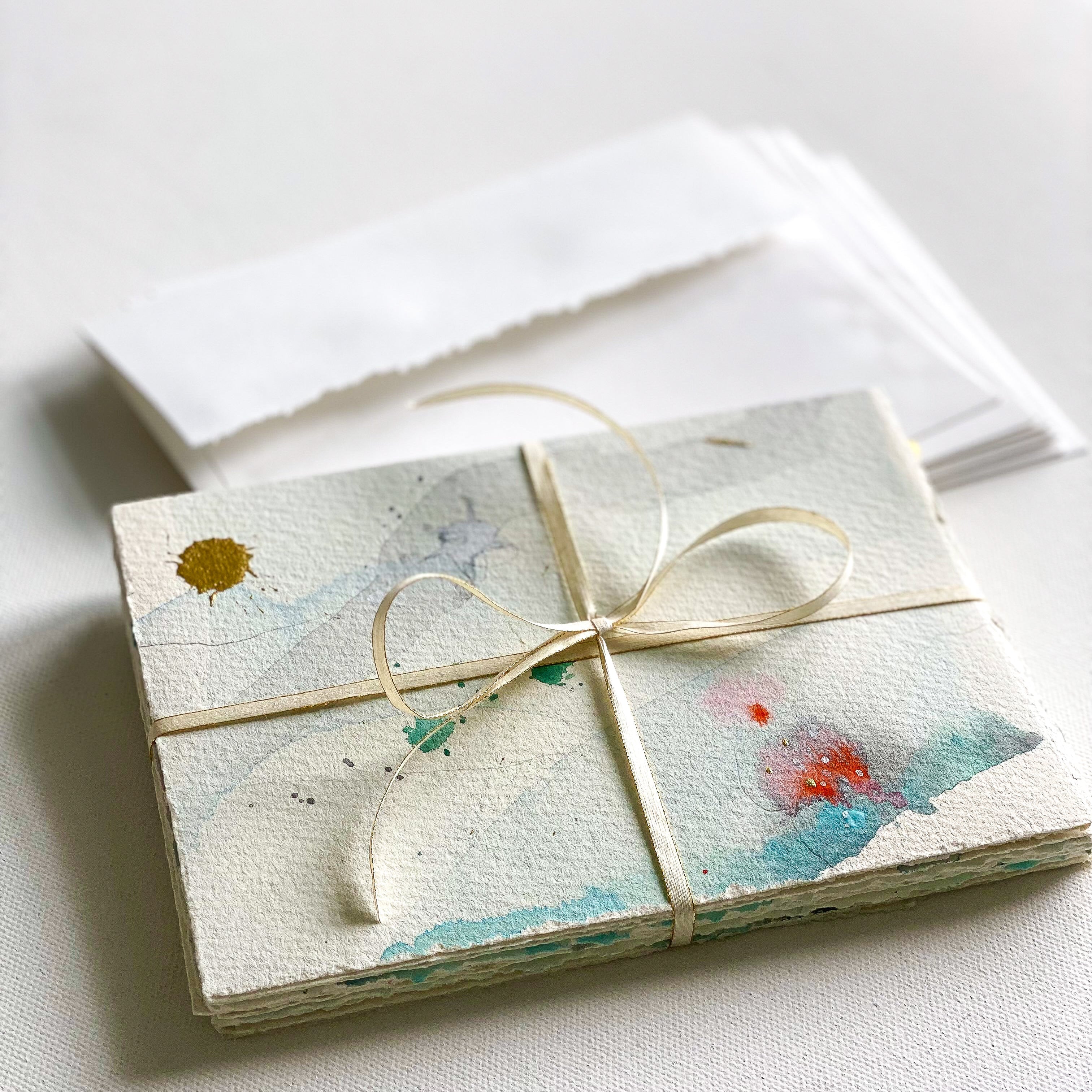 Set of cards with watercolor designs tied with a ribbon on a white surface