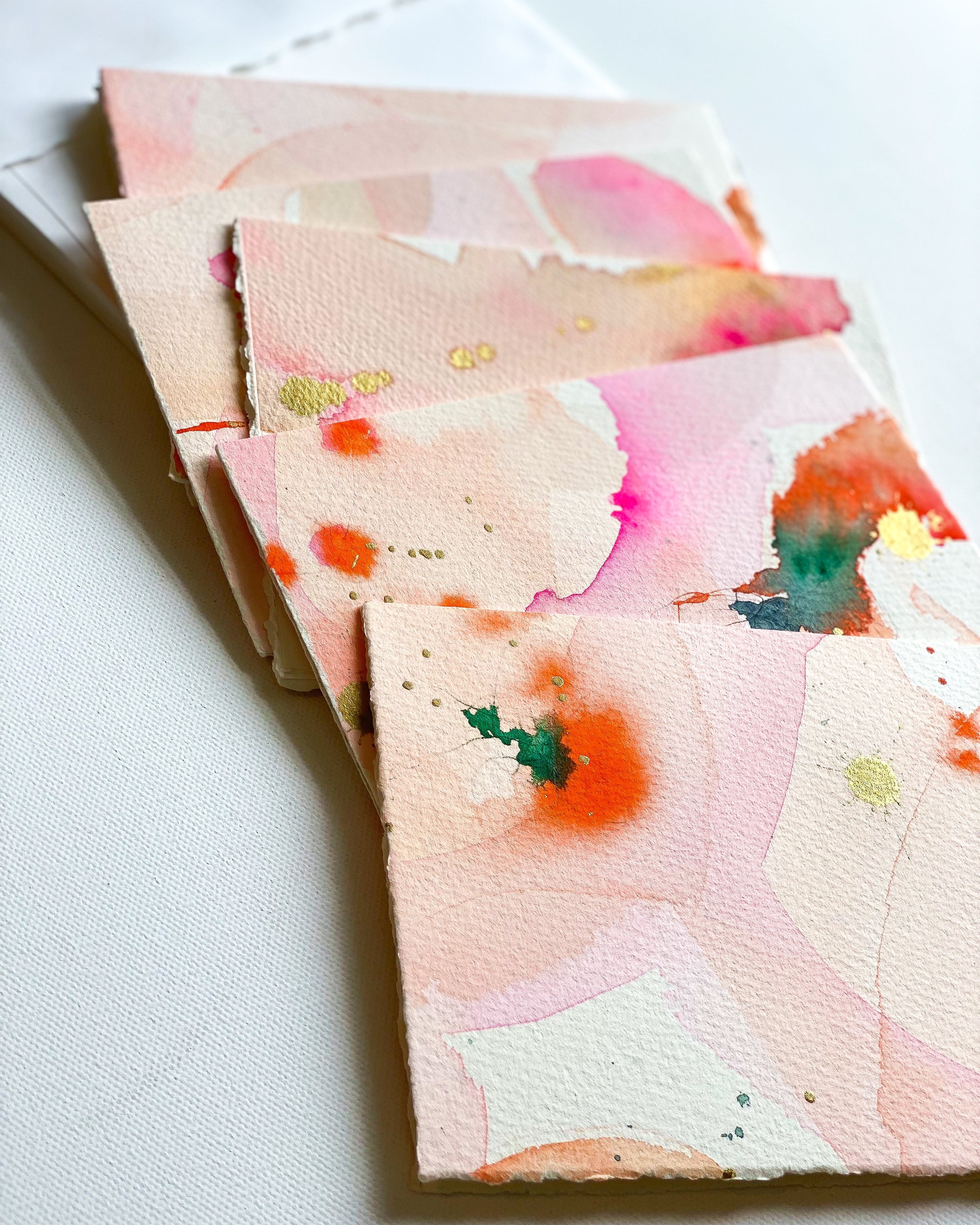 Stack of watercolor cards with abstract designs on a white surface