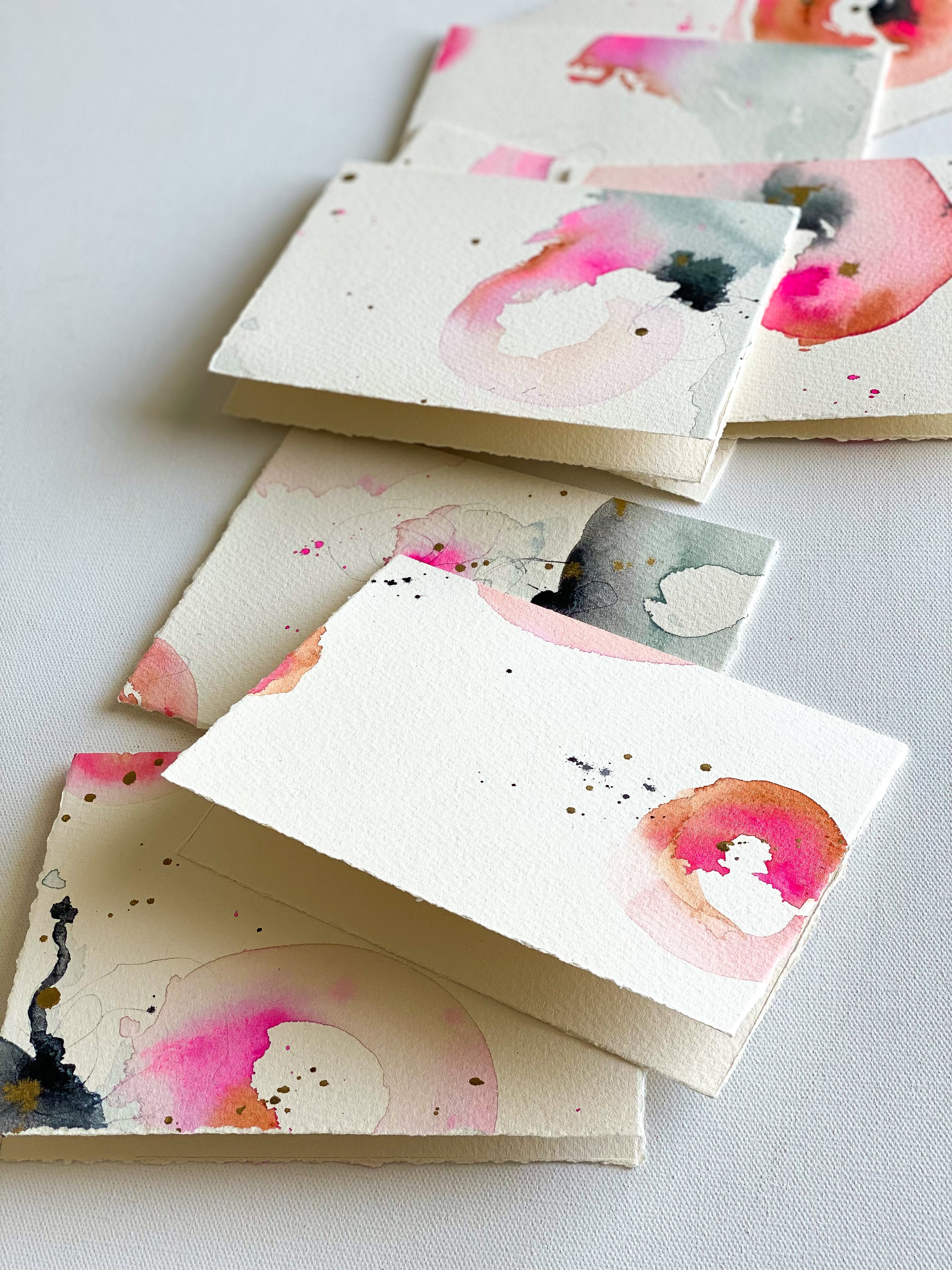 Stack of stationery with watercolor designs on a light gray background